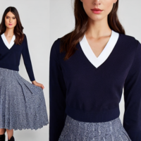 Brunette wearing navy blue v-neck school jumper with a badge logo with white revere blouse and navy blue pleated skirt and navy blue stockings