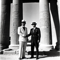 1920s black and white photograph of two explorers, shaking hands in front of an Egyptian temple with hieroglyphics on the walls